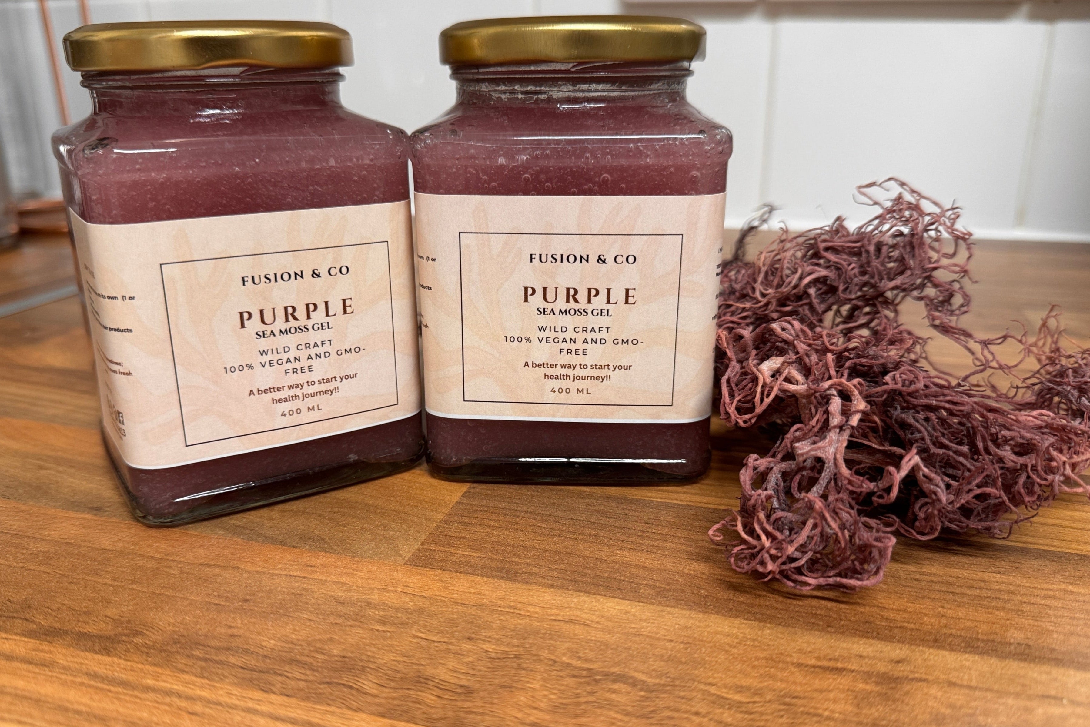 Two jars of 'Purple' sea salt on a wooden surface with seaweed.